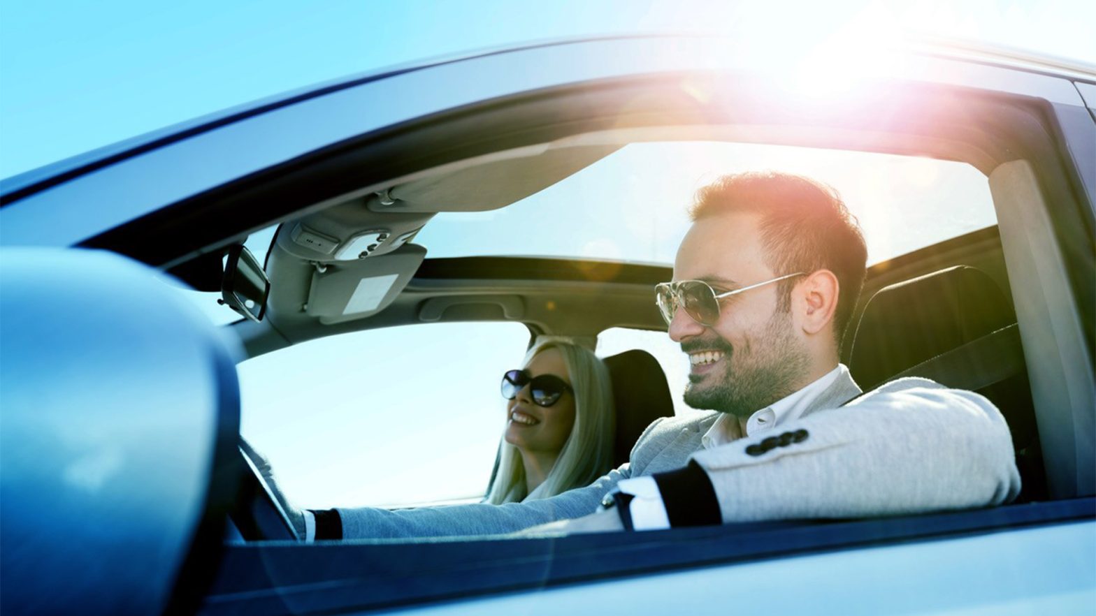 A couple riding in a vehicle while smiling and the sun shinning