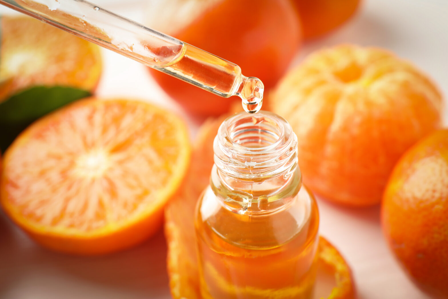 An image of essential oil in a bottle surrounded by oranges.